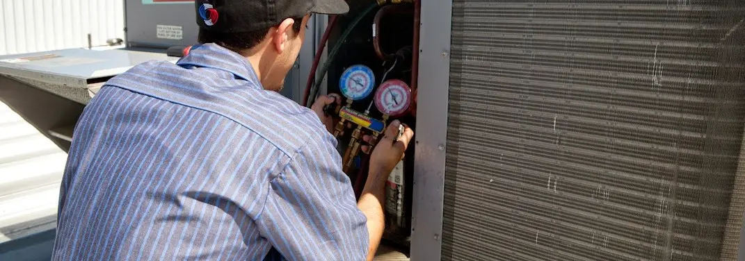 HVAC technician servicing a condenser unit in Troy